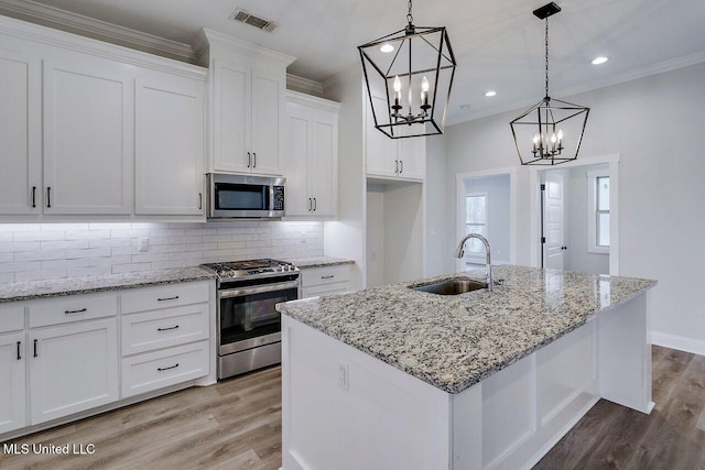 kitchen featuring appliances with stainless steel finishes, decorative light fixtures, white cabinetry, an island with sink, and sink