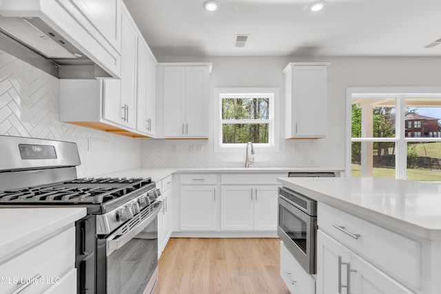 kitchen with light countertops, custom range hood, stainless steel appliances, and visible vents