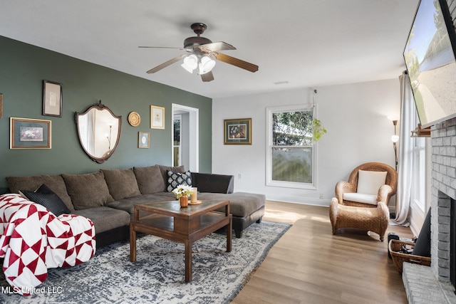 living room featuring ceiling fan, light hardwood / wood-style floors, and a brick fireplace