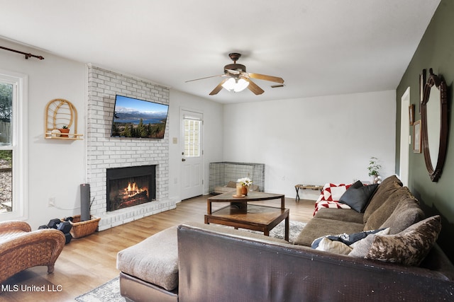 living room with a brick fireplace, ceiling fan, a healthy amount of sunlight, and light hardwood / wood-style floors