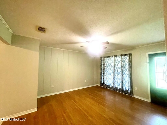 empty room with a textured ceiling, ceiling fan, a healthy amount of sunlight, and dark hardwood / wood-style floors