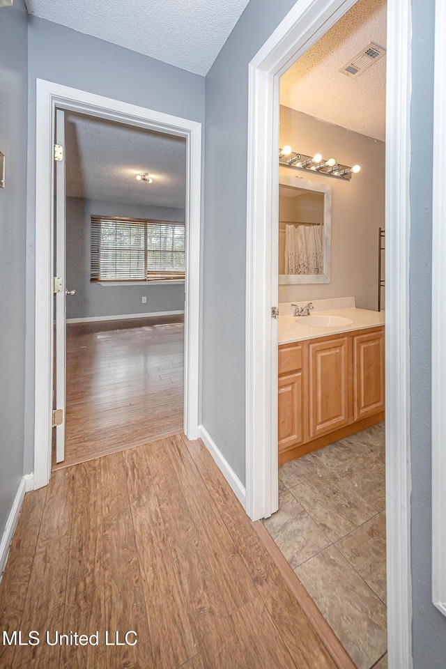 8113 Barron Rd, Moss Point, MS 39562 - hall featuring a textured ceiling, light wood-type flooring, a sink, and baseboards