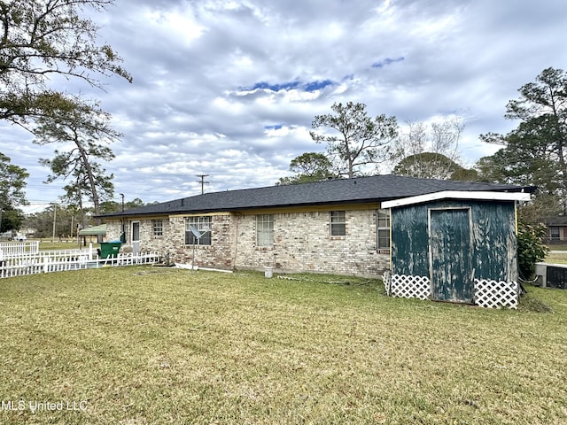 back of house featuring central air condition unit, brick siding, fence, and a yard