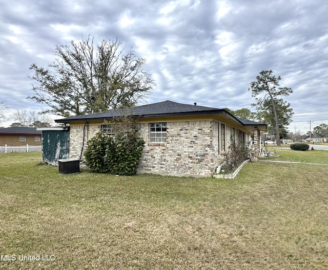 view of side of home featuring brick siding, fence, and a yard