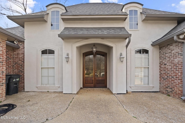 doorway to property with brick siding, a shingled roof, and stucco siding