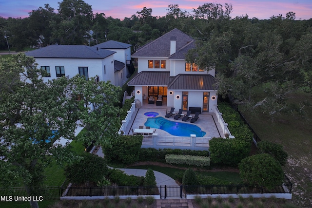 back house at dusk featuring a patio and a fenced in pool