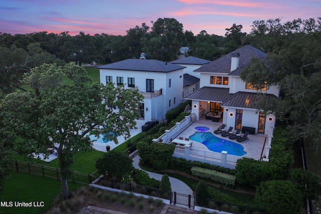 back house at dusk featuring a patio and a fenced in pool