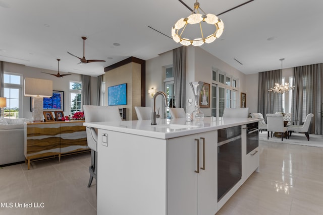 kitchen featuring sink, an island with sink, white cabinetry, pendant lighting, and an inviting chandelier