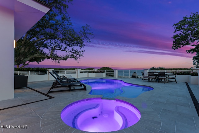 pool at dusk featuring an in ground hot tub, a patio, and a water view