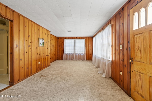 foyer featuring visible vents, light colored carpet, and wooden walls