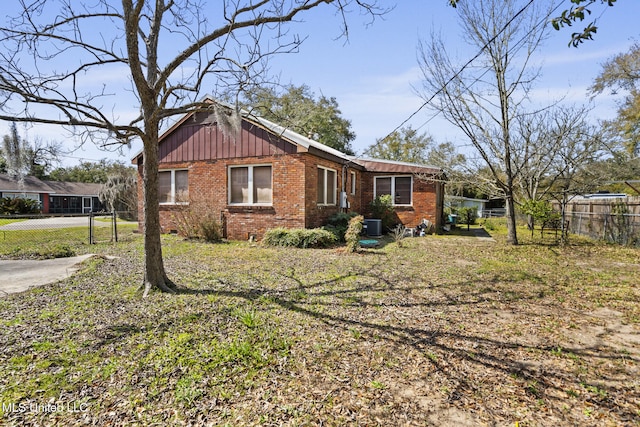 view of front of house featuring brick siding, central air condition unit, board and batten siding, and fence