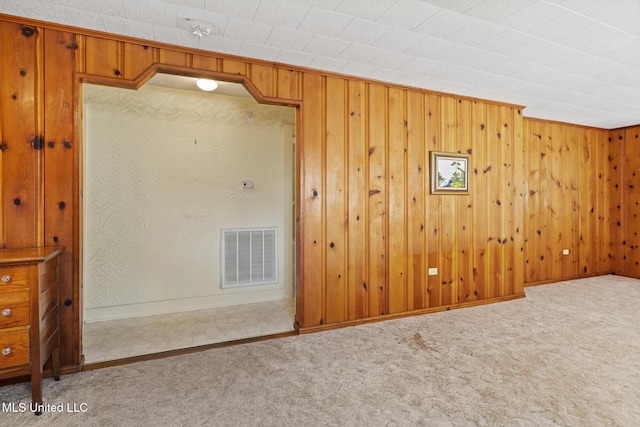 carpeted empty room featuring visible vents, baseboards, and wooden walls