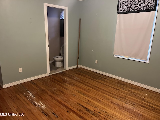unfurnished bedroom with ensuite bath, wood-type flooring, and baseboards