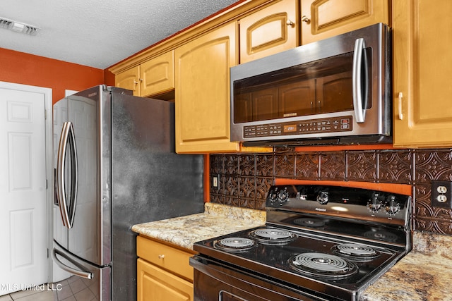 kitchen featuring appliances with stainless steel finishes, a textured ceiling, light stone counters, decorative backsplash, and tile patterned flooring