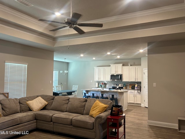 living room with crown molding, a tray ceiling, ceiling fan with notable chandelier, and hardwood / wood-style floors