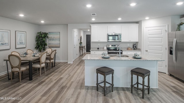169 Mill Ct, Lucedale, MS 39452 - kitchen with appliances with stainless steel finishes, light wood-style floors, a kitchen island with sink, a kitchen bar, and light stone counters