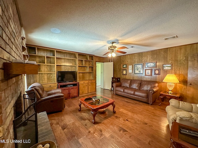 living room with ceiling fan, wood walls, a textured ceiling, and hardwood / wood-style floors