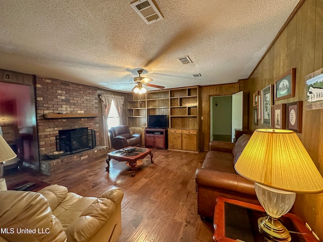 living room featuring wood walls, hardwood / wood-style floors, a textured ceiling, a fireplace, and ceiling fan