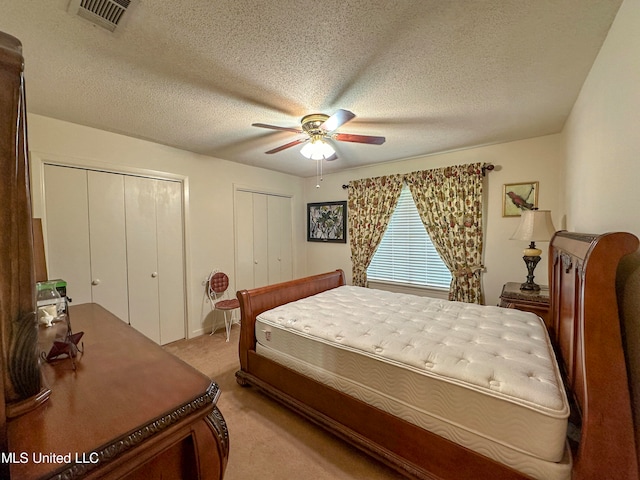 carpeted bedroom featuring multiple closets, a textured ceiling, and ceiling fan