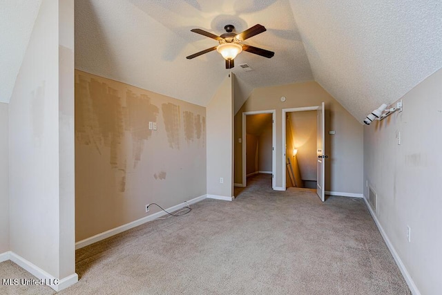 unfurnished bedroom featuring ceiling fan, light colored carpet, a textured ceiling, and lofted ceiling