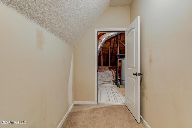 hallway featuring a textured ceiling, water heater, lofted ceiling, and light carpet