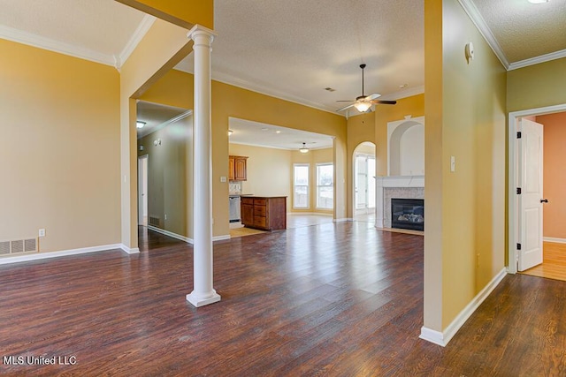 unfurnished living room featuring dark wood-type flooring, ornate columns, ornamental molding, ceiling fan, and a tile fireplace