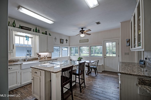 kitchen with sink, a breakfast bar, a healthy amount of sunlight, a kitchen island, and white cabinets