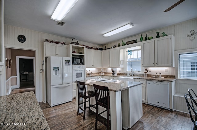 kitchen with white cabinetry, light stone countertops, dark hardwood / wood-style floors, white appliances, and a kitchen island