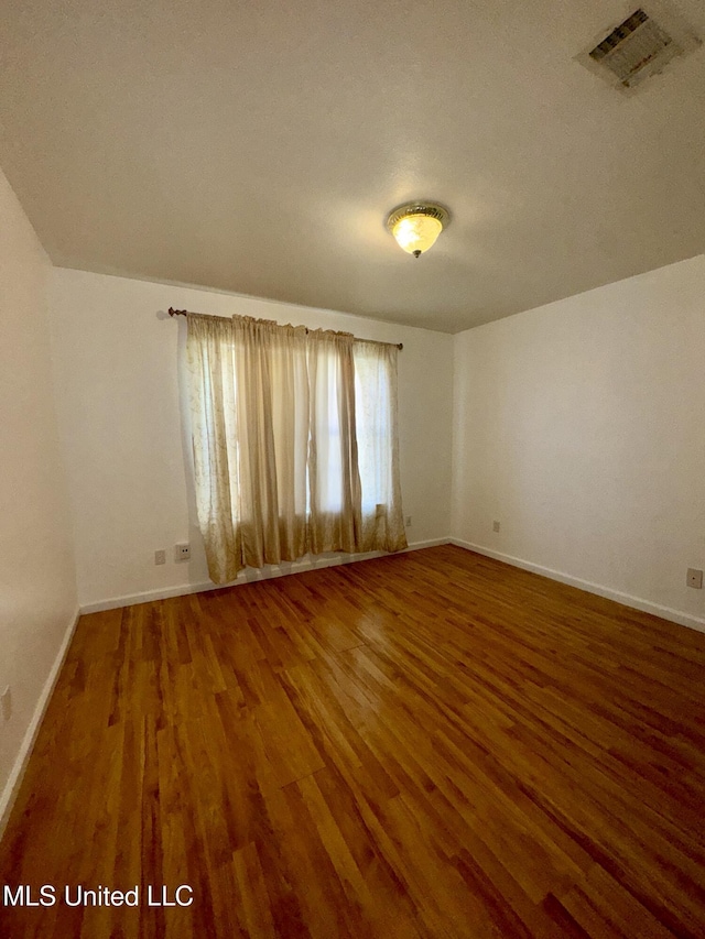 spare room featuring visible vents, baseboards, and wood finished floors