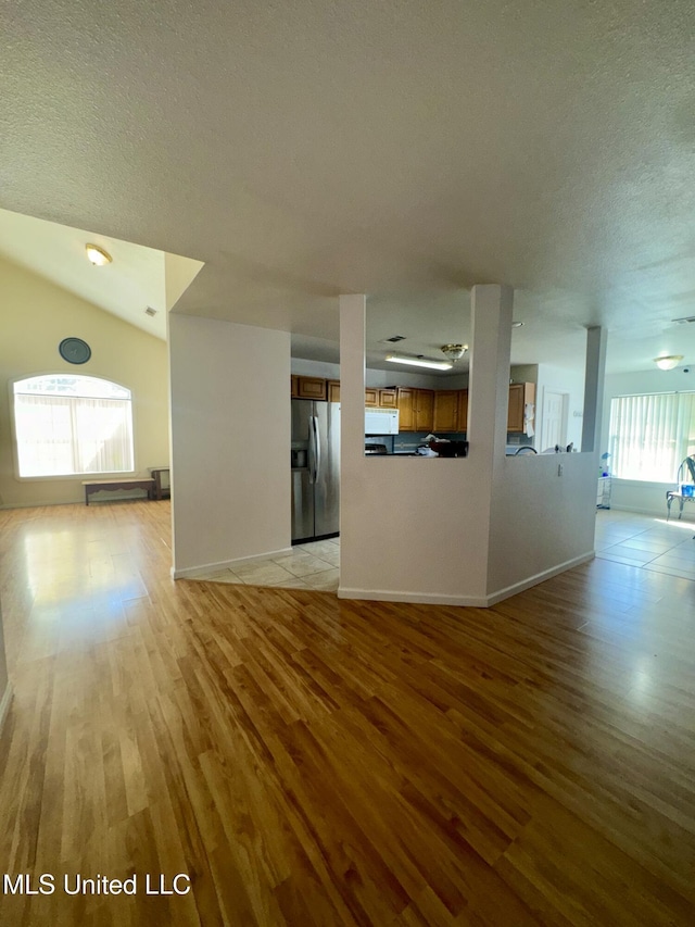 unfurnished living room with light wood finished floors, a textured ceiling, and baseboards