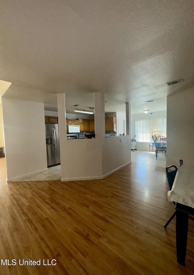 unfurnished living room with visible vents, light wood-style flooring, a textured ceiling, and baseboards