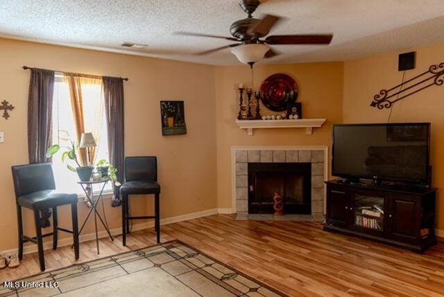 living room with a textured ceiling, a tiled fireplace, wood-type flooring, and ceiling fan