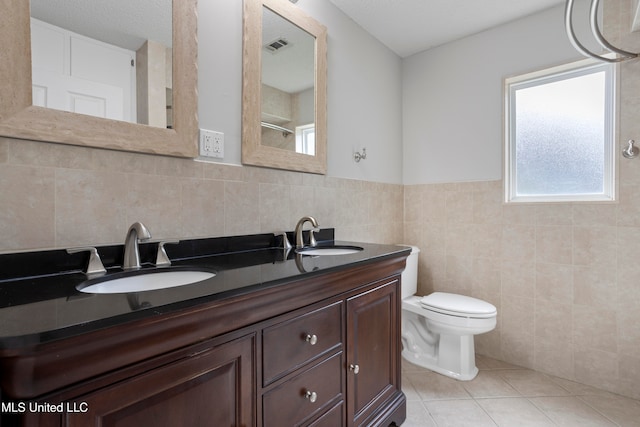 bathroom with tile patterned floors, a textured ceiling, vanity, tile walls, and toilet