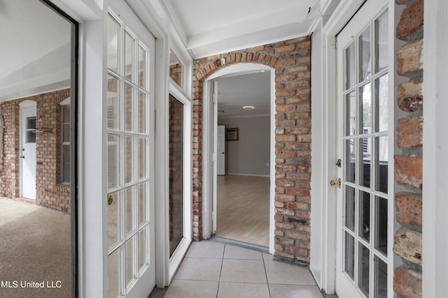 hallway featuring crown molding, french doors, light hardwood / wood-style floors, and brick wall