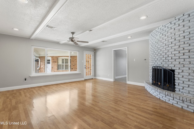 unfurnished living room featuring hardwood / wood-style flooring, ceiling fan, a fireplace, a textured ceiling, and beamed ceiling