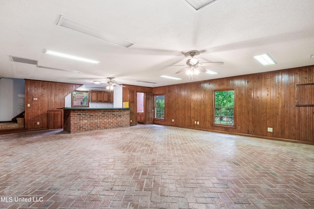 unfurnished living room featuring ceiling fan, wood walls, and a textured ceiling