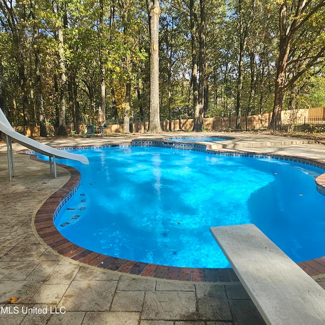 view of swimming pool featuring a diving board, a patio area, a water slide, and a hot tub