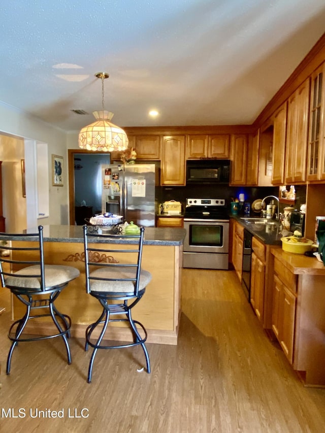 kitchen with brown cabinetry, light wood finished floors, a sink, black appliances, and dark countertops