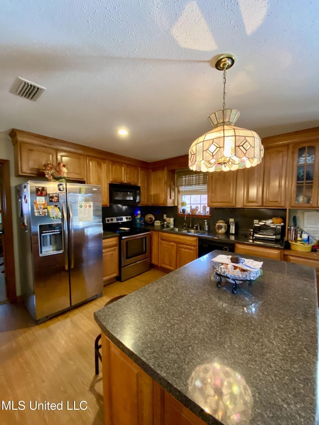 kitchen featuring visible vents, brown cabinets, black appliances, light wood finished floors, and glass insert cabinets