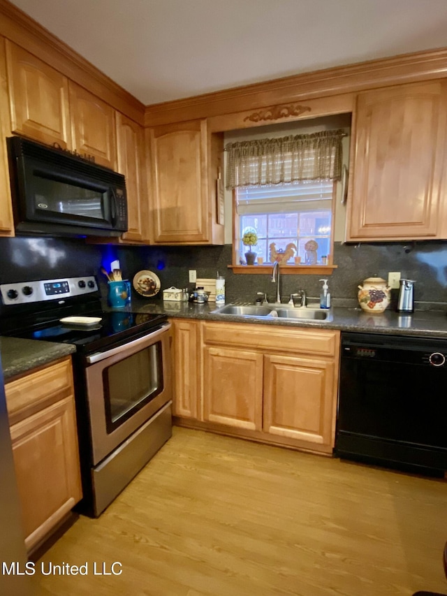 kitchen featuring black appliances, a sink, dark countertops, backsplash, and light wood-style floors