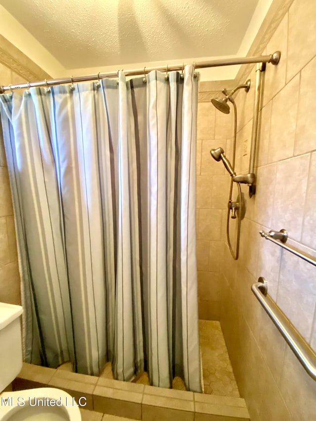 full bathroom with a textured ceiling, toilet, and a tile shower