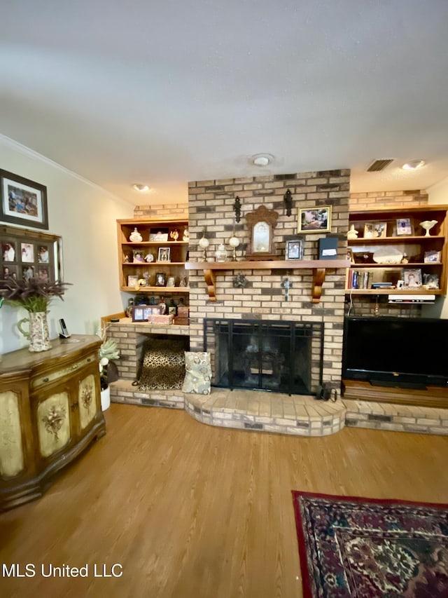 living room with visible vents, wood finished floors, a fireplace, and ornamental molding