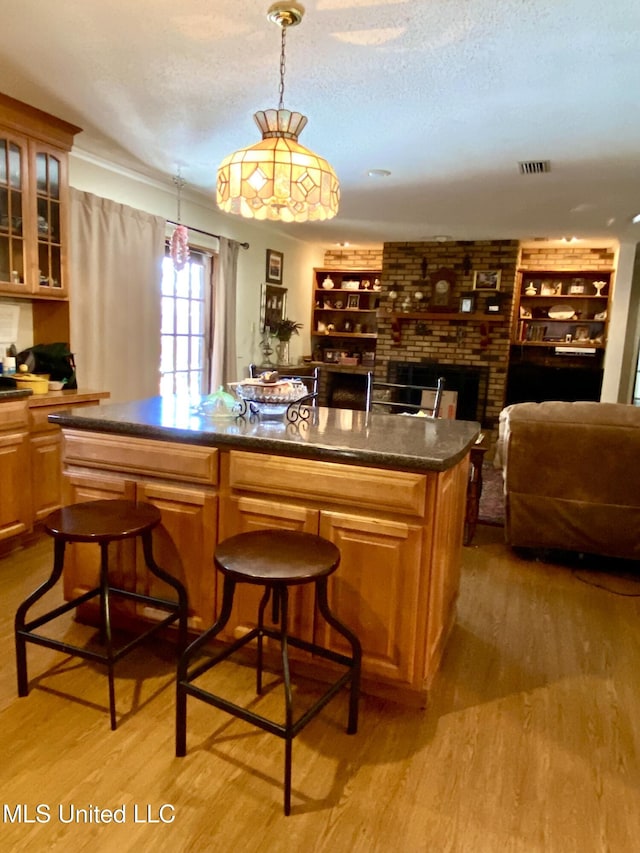 bar featuring visible vents, pendant lighting, a textured ceiling, light wood finished floors, and a brick fireplace