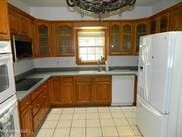 kitchen with a sink, brown cabinets, white appliances, glass insert cabinets, and light tile patterned floors