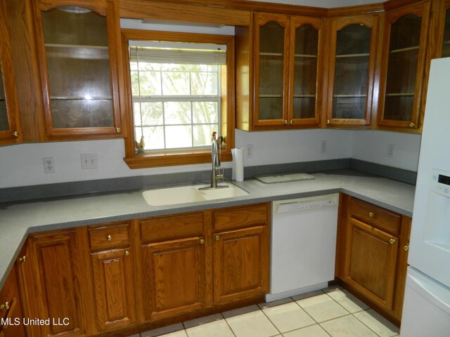 kitchen featuring brown cabinetry, glass insert cabinets, a sink, and white appliances