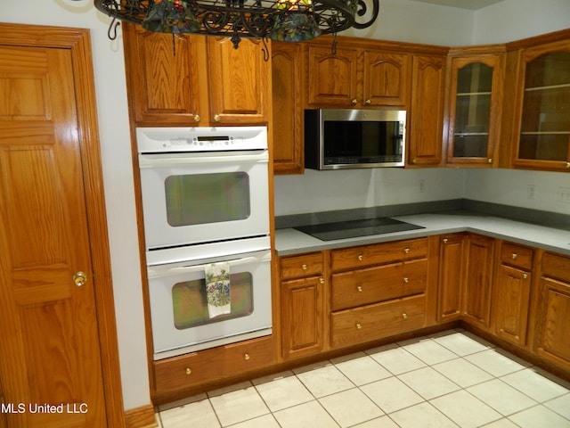 kitchen with stainless steel microwave, glass insert cabinets, brown cabinets, black electric stovetop, and double oven