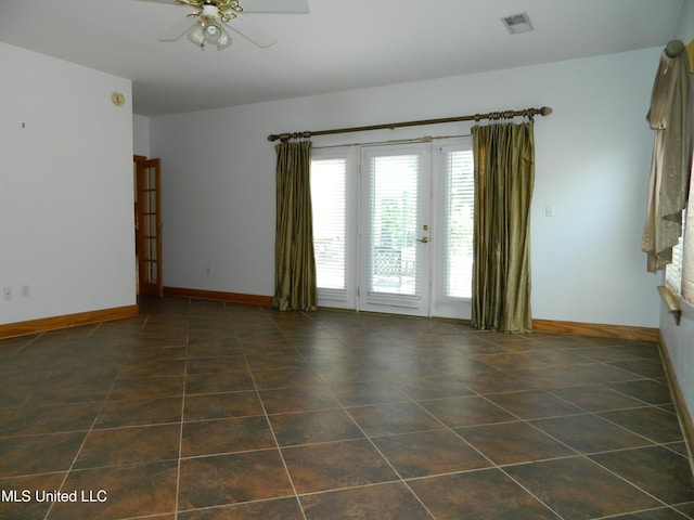 empty room featuring baseboards, visible vents, dark tile patterned floors, and ceiling fan