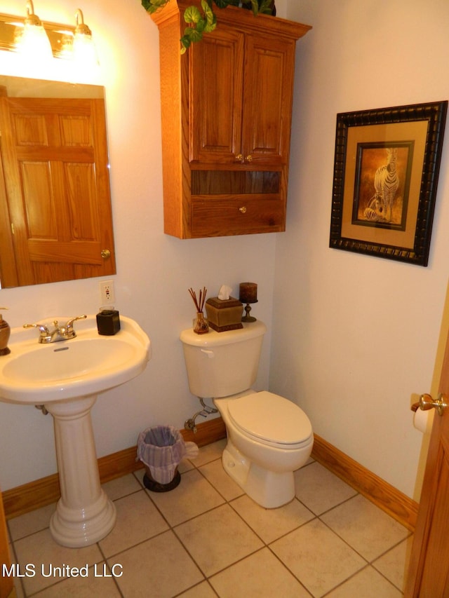 half bath with baseboards, tile patterned flooring, and toilet