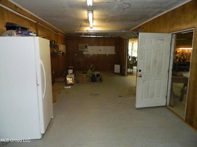 basement with a garage, crown molding, wooden walls, and freestanding refrigerator