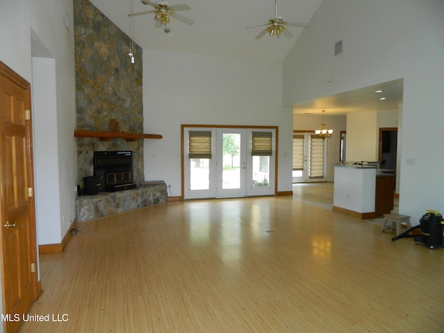 unfurnished living room with light wood-style floors, baseboards, high vaulted ceiling, and ceiling fan with notable chandelier